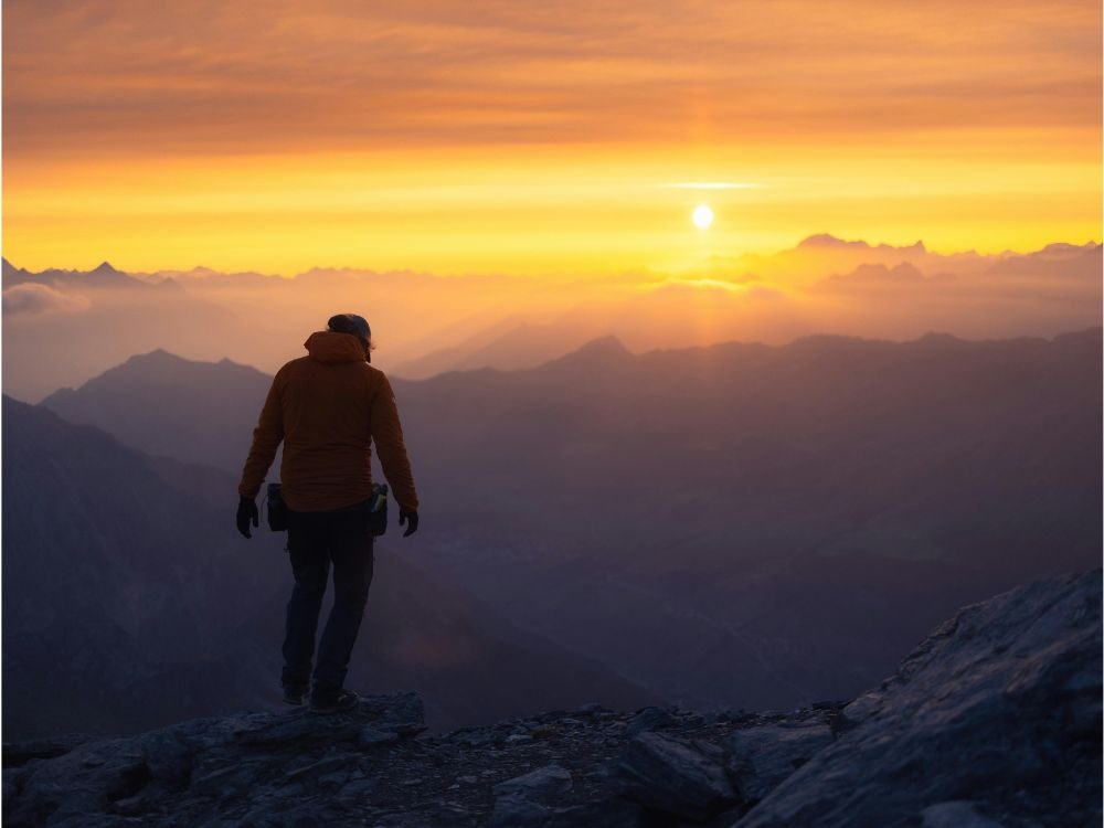 Pessoa caminhando no topo de uma montanha ao pôr do sol, simbolizando superação e jornada de crescimento.