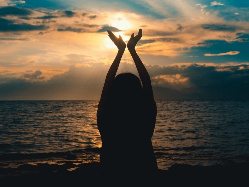 pessoa com braços erguidos diante do pôr do sol, representando conexão espiritual e esperança.